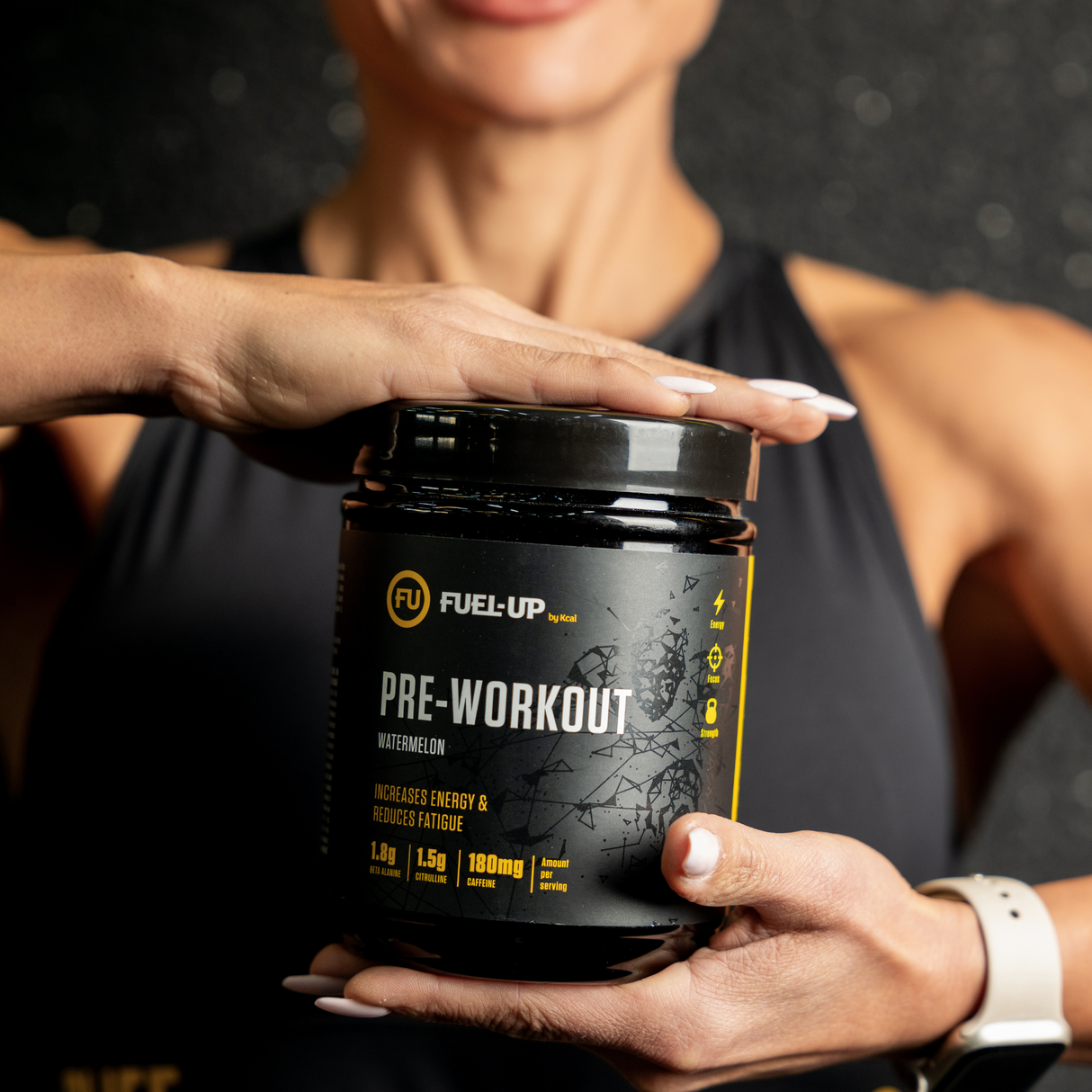 Woman in sports top holding a container of pre-workout supplements in the gym